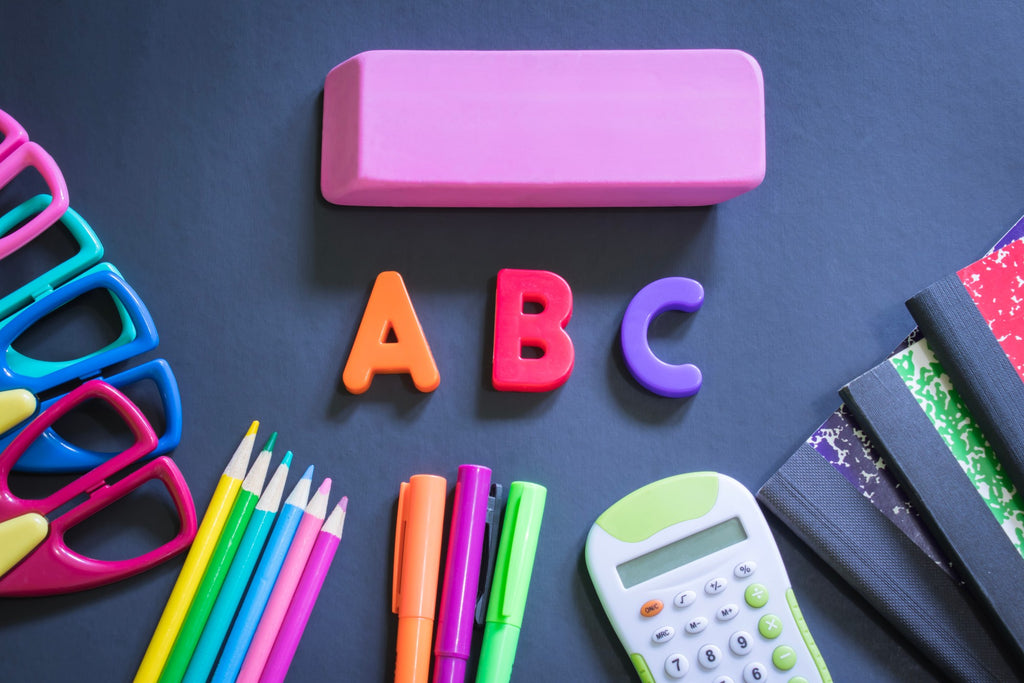 Back to school supplies including scissors, a calculator, notebooks, erasers, pens and pencils around ABC magnets.