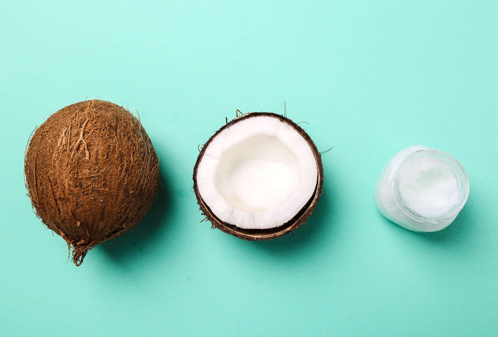 Whole coconut, Half-cut coconut, and coconut oil in a jar with a bright cyan background 