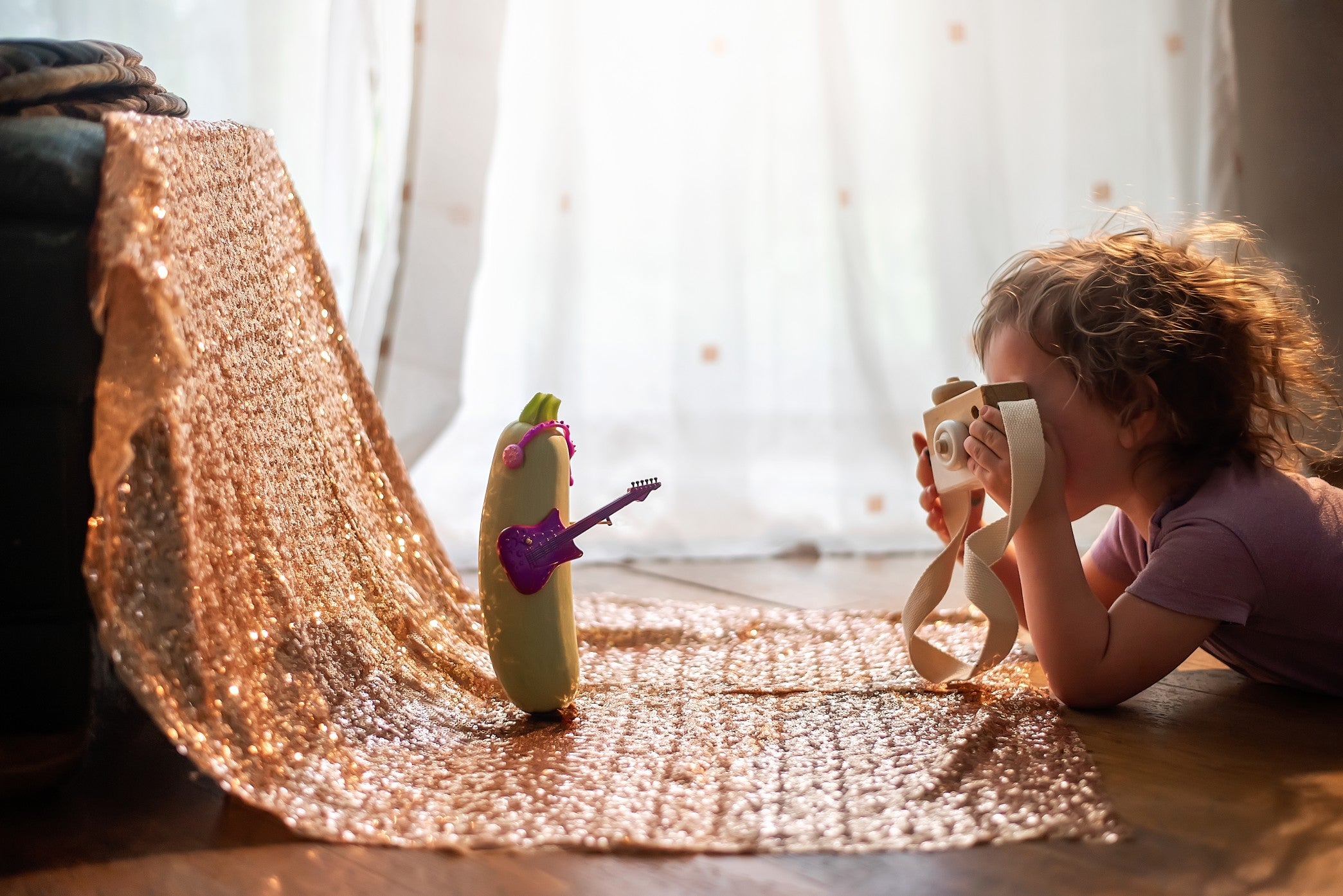 Little girl photographs with wooden toy camera a glamorous vegetable marrow with guitar headphones