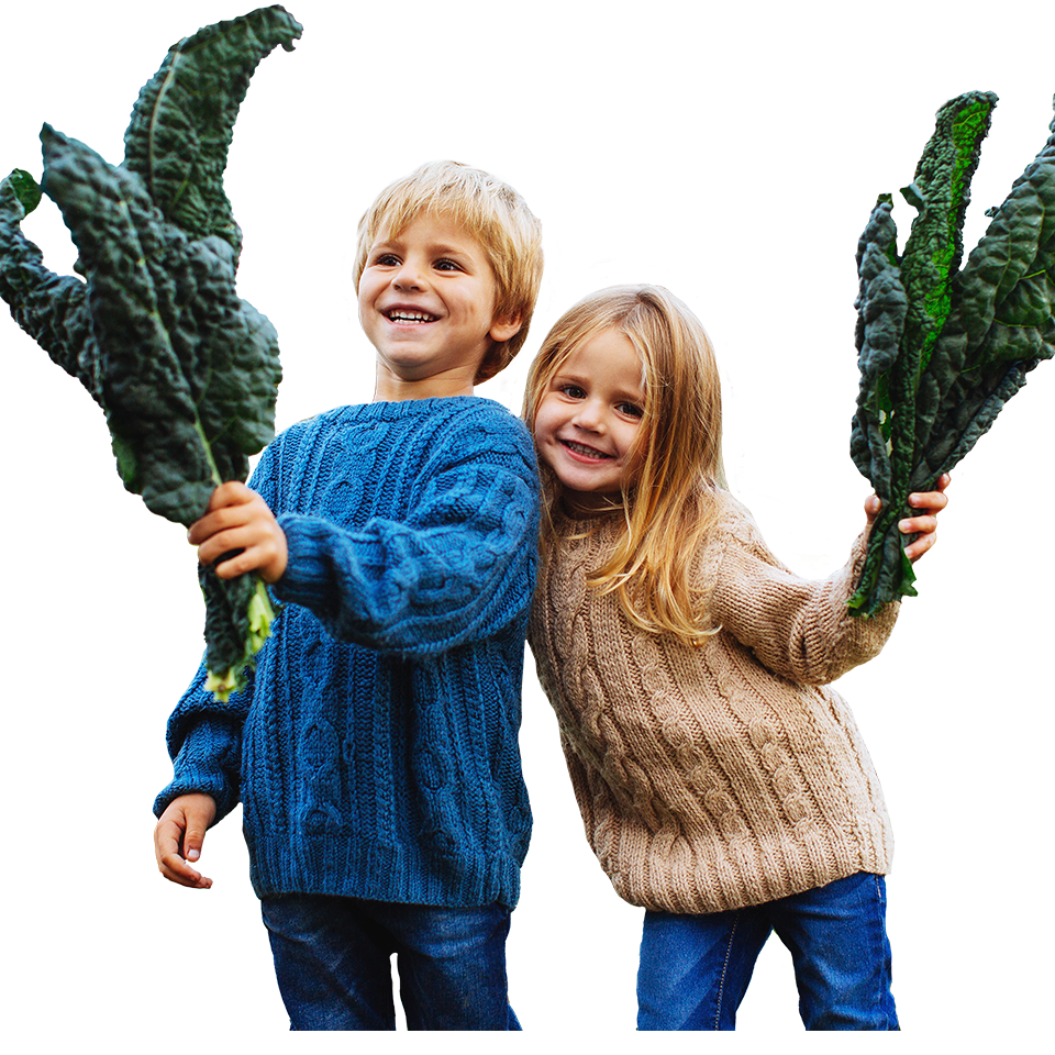two smiling kids holding kale leaves