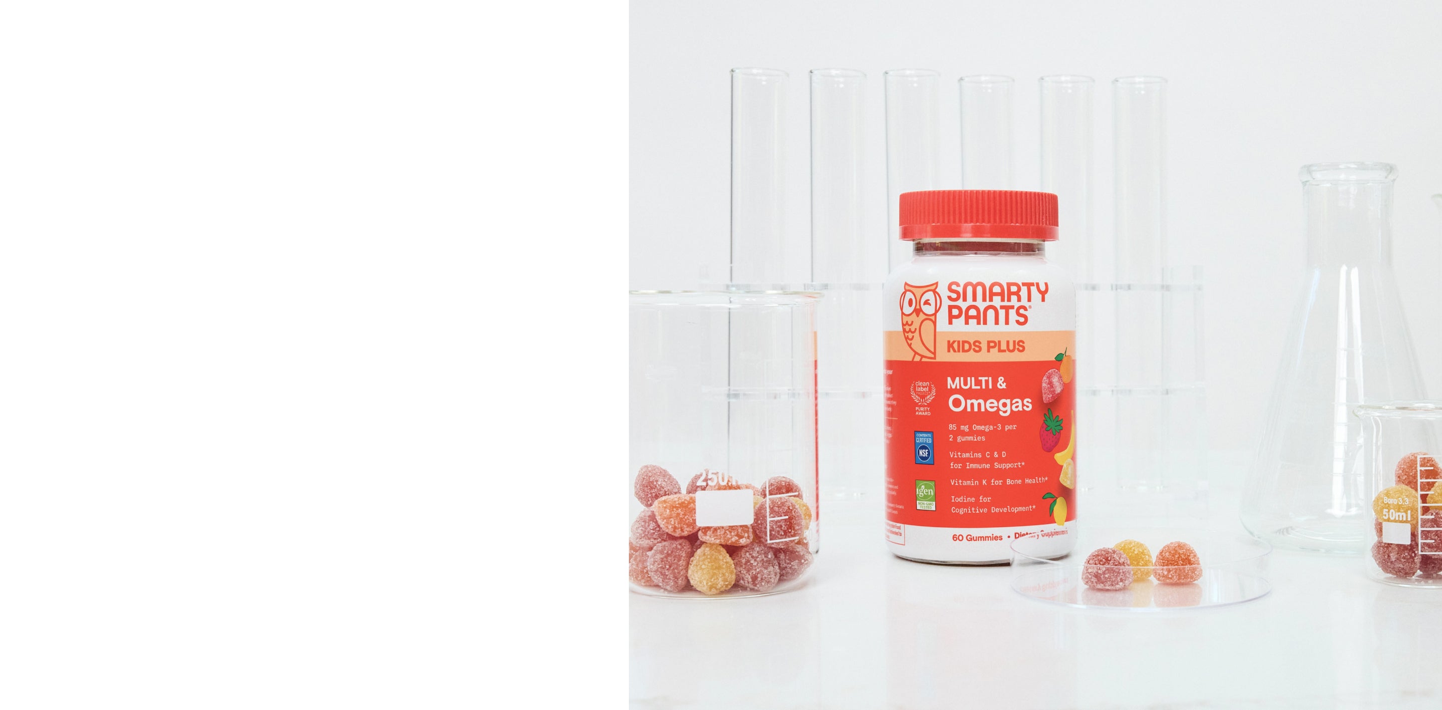 A bottle of Smarty Pants Kids Plus Multi & Omega 3 gummy vitamins stands on a white surface with clear glass beakers and candy pieces around it against a white paneled background.