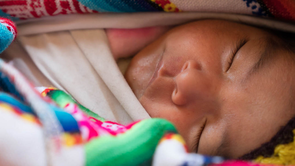 Newborn baby sleeping peacefully with colorful blankets and toys around